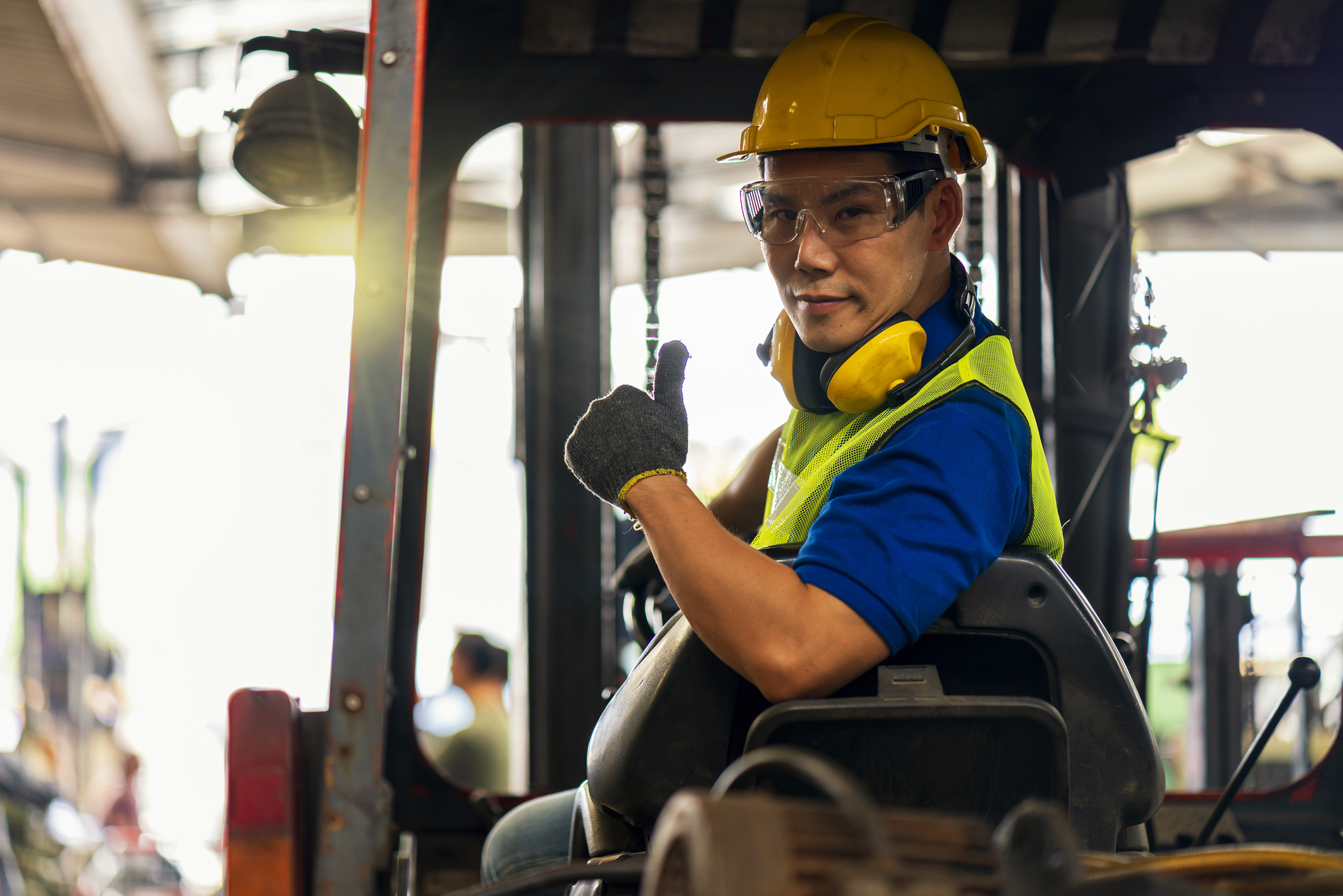 Engineer or technician Concept. A male employee driving a forklift and showing thumb up in factory.